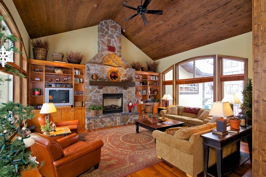 A comfortble, classic traditional ski chalet styled living room with a stone fireplace, comfortable seating, and wood panelled ceiling.