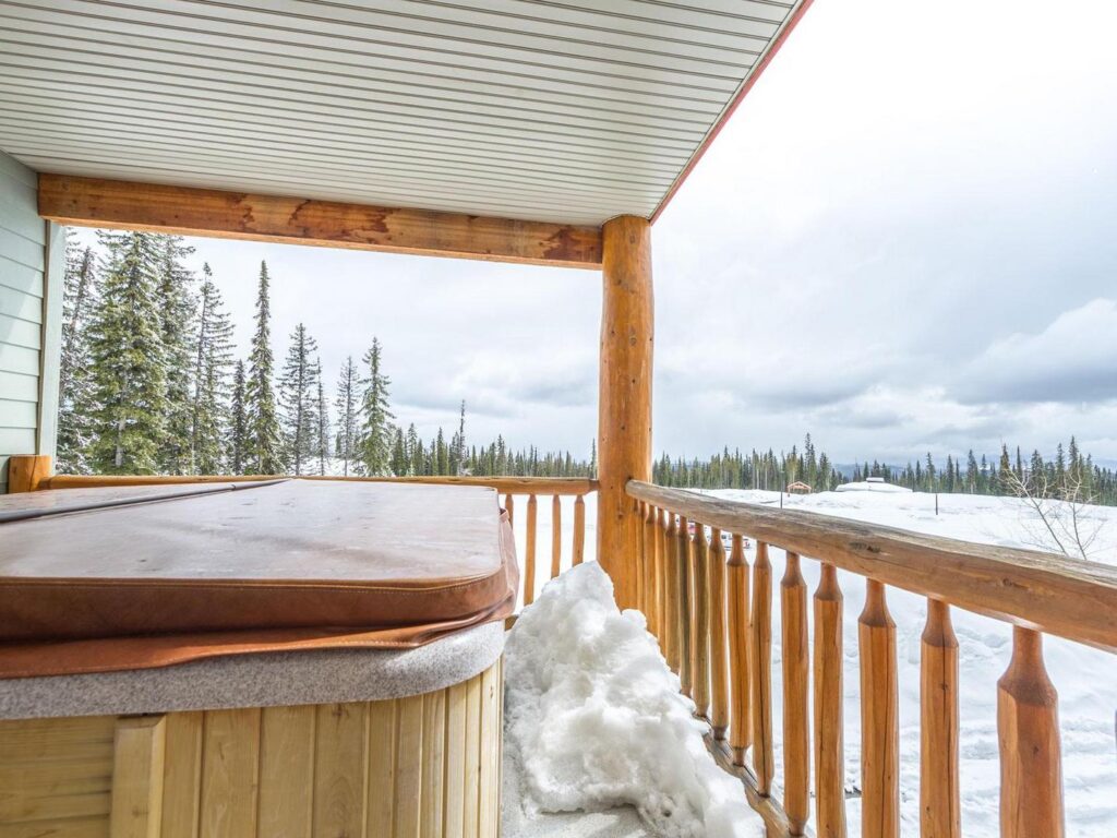 The view off the balcony of one of the Spyglass luxury vacation rental units, with log-style pillars and railing and a hot tub, managed by Luxury Mountain Vacation Rentals at Big White Ski Resort.