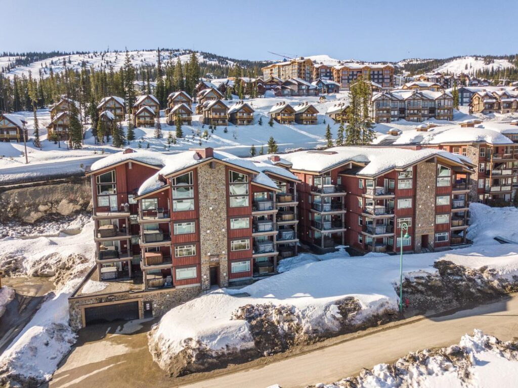 The outside of the Raven building with snow around it on a sunny day, located at Big White Ski Resort and managed by Luxury Mountain Vacation Rentals.