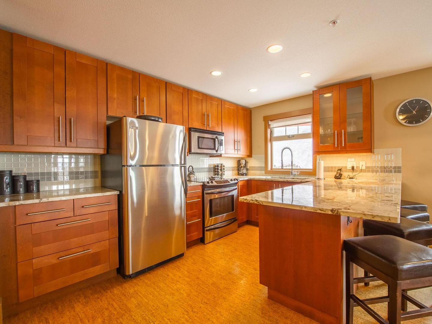 Raven 209's fully equipped gourtment kitchen with warm coloured wooden cabinets, marble countertops and stainless steel appliances in a luxury vacation rental condo managed by Luxury Mountain Vacation Rentals at Big White Ski Resort.