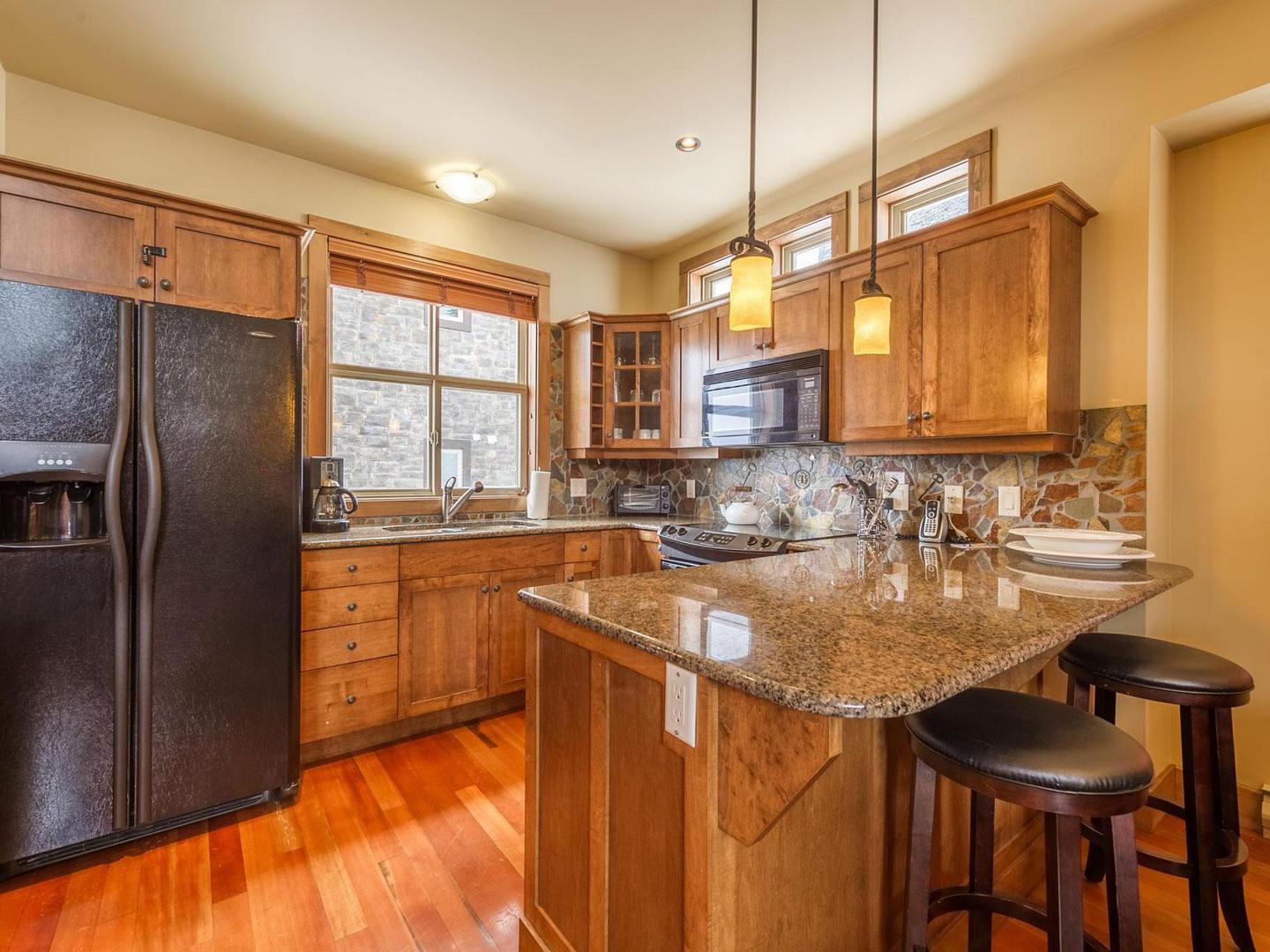 The open concept gourmet kitchen with hardwood floors and warm, wood accents in luxury vacation rental South Point #15 at Big White Ski Resort.