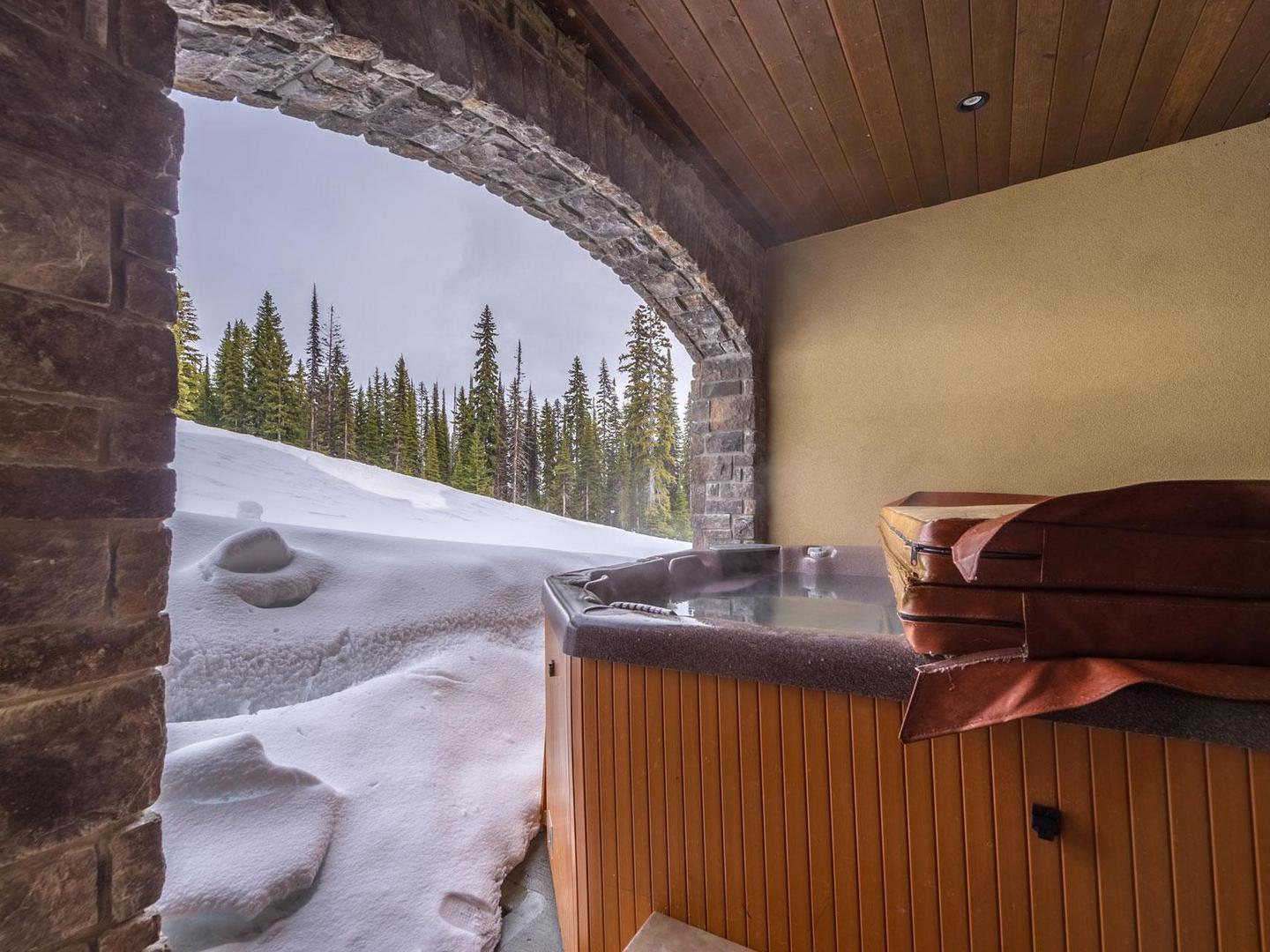 The private deck and hot tub with stone accents and snow nearby at luxury vacation rental South Point #15 at Big White Ski Resort.