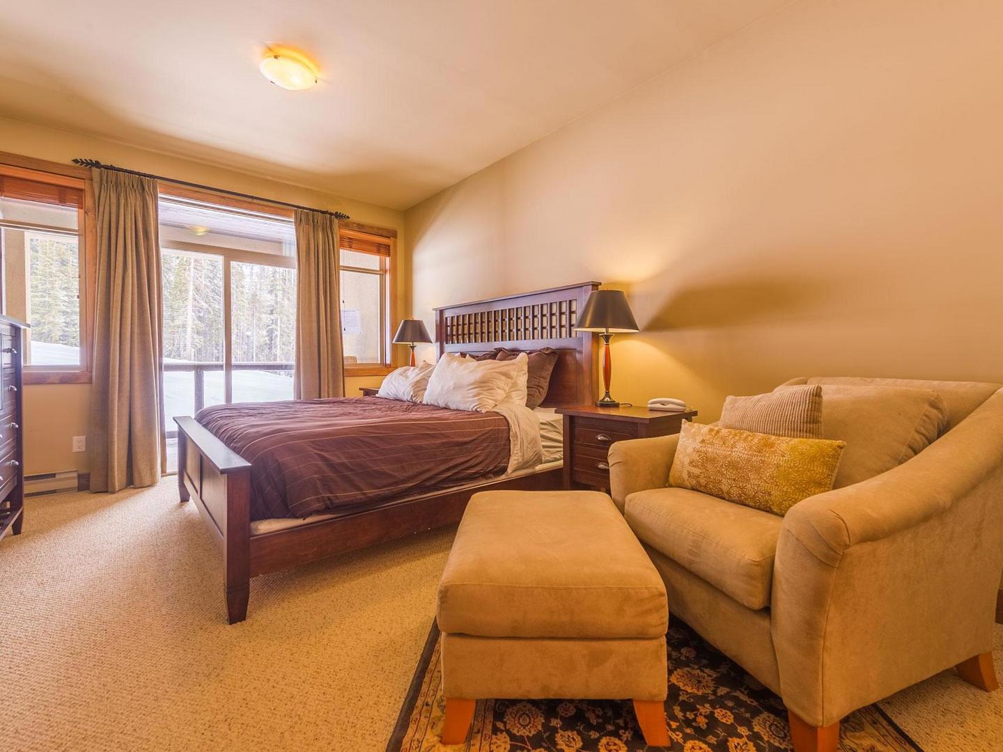 The master bedroom suite with a cofmortable seating area, warm natural light and a comfortable bed in luxury vacation rental South Point #15 at Big White Ski Resort.