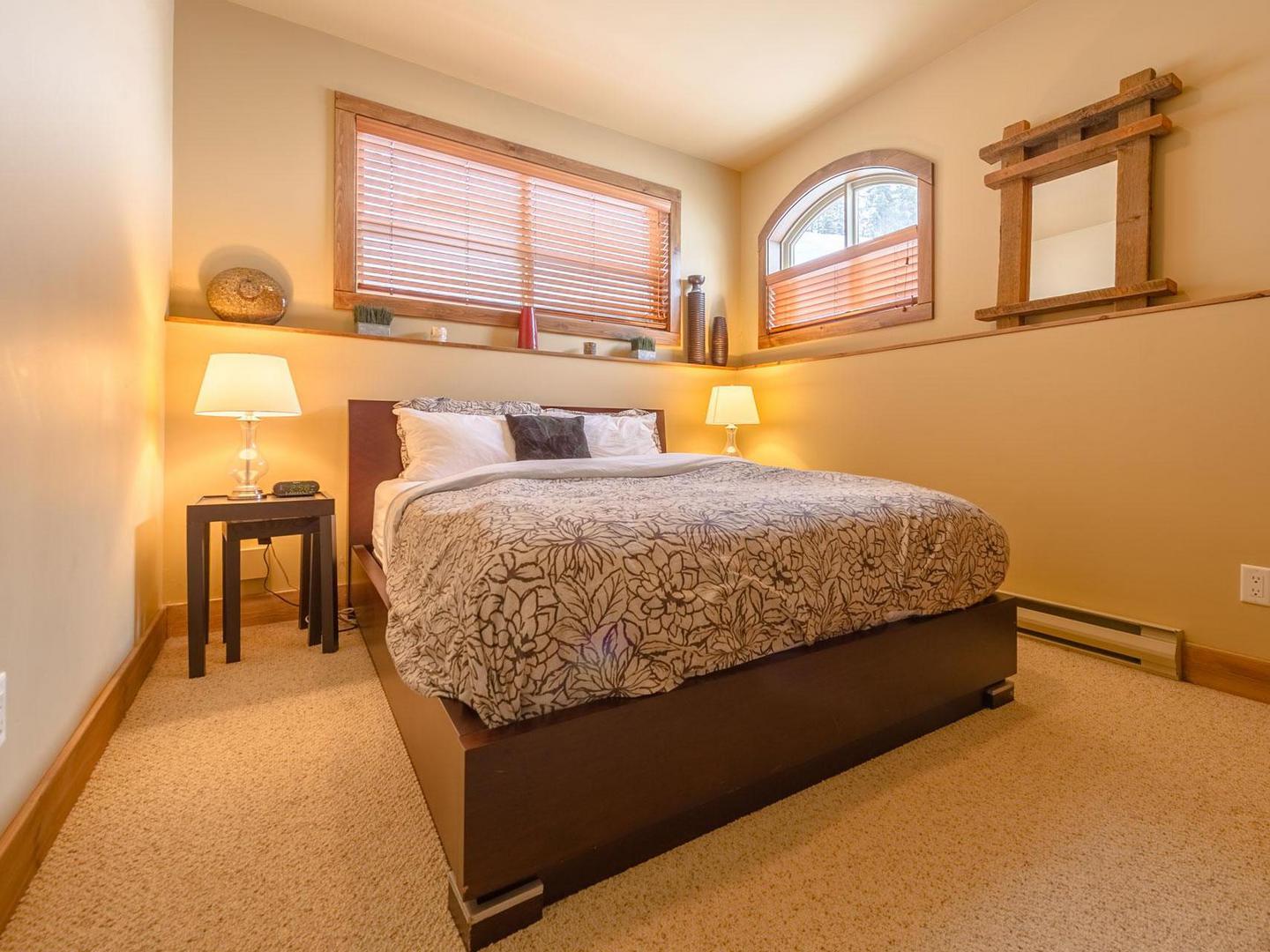 The queen bedroom suite with a cozy bedroom, carpeted floors and warm lighting in luxury vacation rental in South Point #15 at Big White Ski Resort.