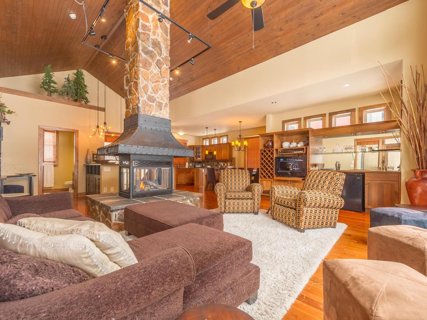 The open concept living room, kitchen and dining room, with a free standing fireplace as the focal point, with wood and stone accents in South Point #15 at Big White Ski Resort.