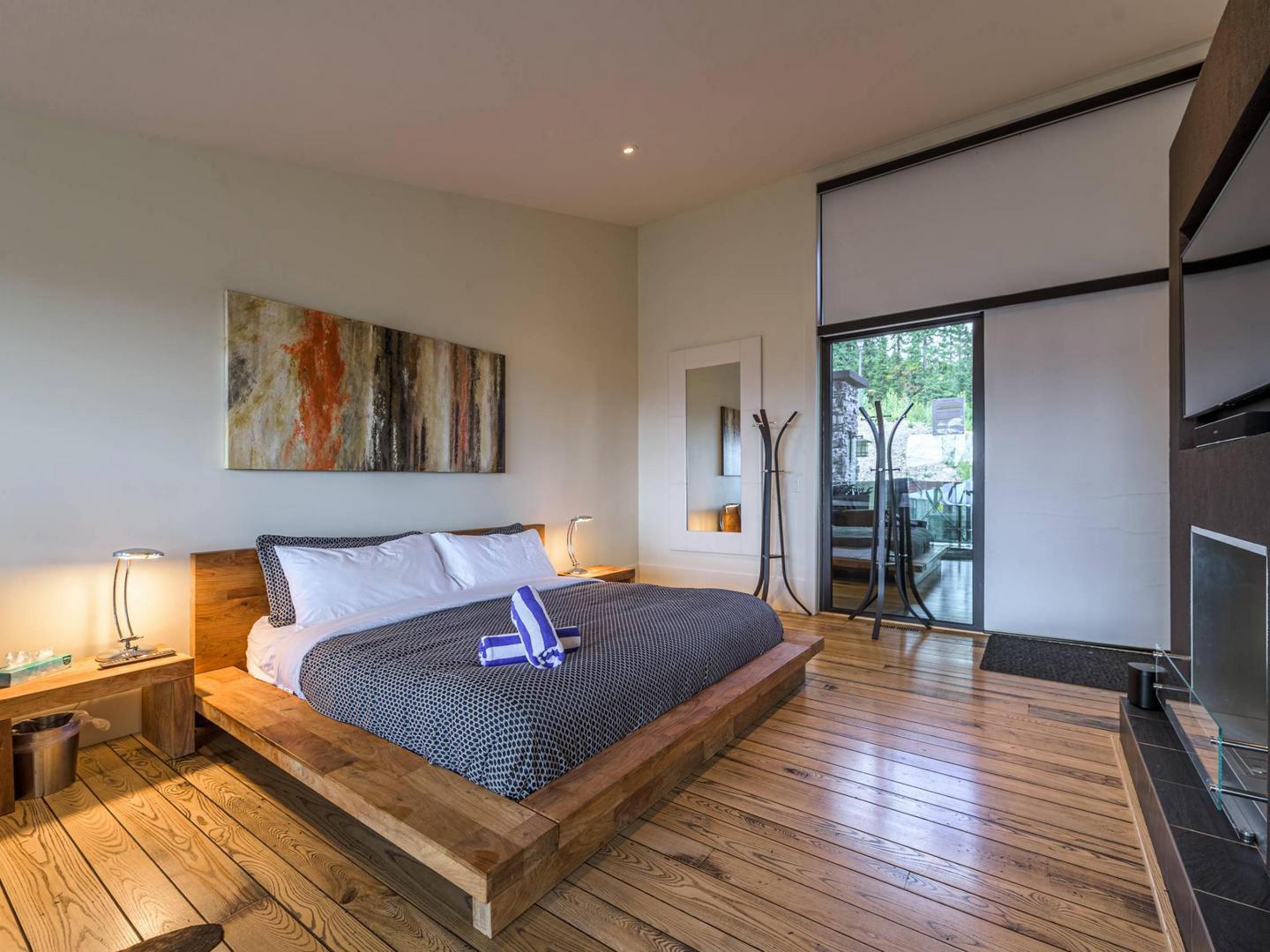 The grand master kind bedroom with hardwood floors, comfortable furnishings nad bedding, bright natural light, and a cozy fireplace in the Edge #7 at Big White Ski Resort.