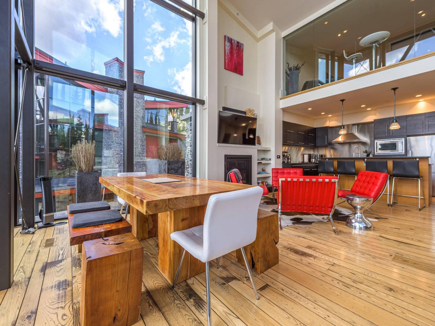 The open concept dining area with the kitchen and living room in the background and huge floor to ceiling windows surrounding it, with modern luxury finishes in the Edge #7 at Big White Ski Resort.