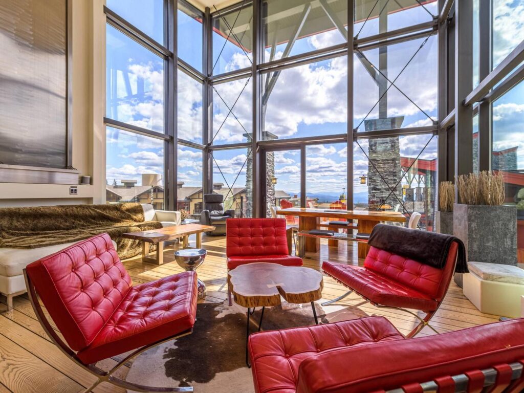 Four red leather chairs surround a wooden coffee table in a luxury, modern living room with hardwood floors and floor to ceiling windows with stunning views of Big White Ski Resort in a luxury rental from Luxury Mountain Vacation Rentals.