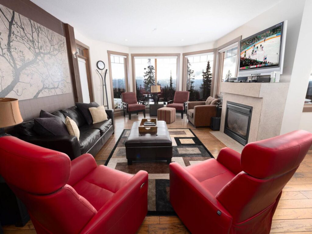 The living room in one of the Timbers' luxury vacation rental condos, with red and black leather seats and coaches, a cozy fireplace, large panoramic windows, and a Christmas tree in the corner for a nostalgic ski chalet feel in December. Managed by Luxury Mountain Vacation Rentals at Big White Ski Resort.