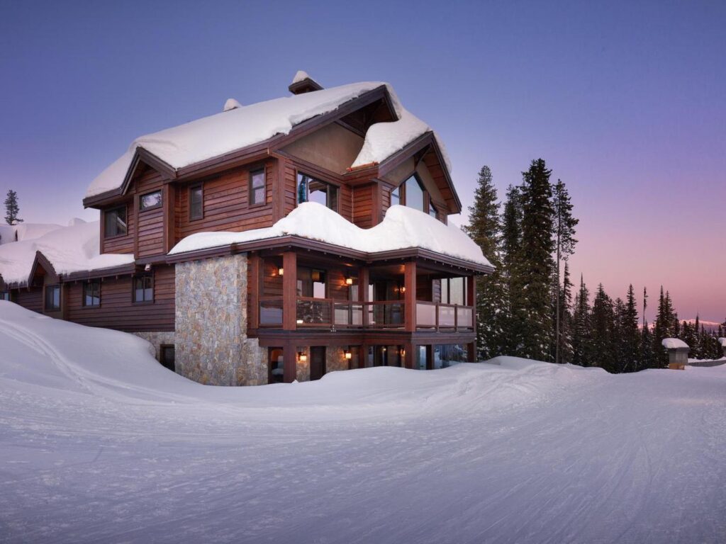 The exterior of the luxury White Caviar Chalet at Big White Ski Resort with purple blue skies above and blankets of champagne powder snow around it.