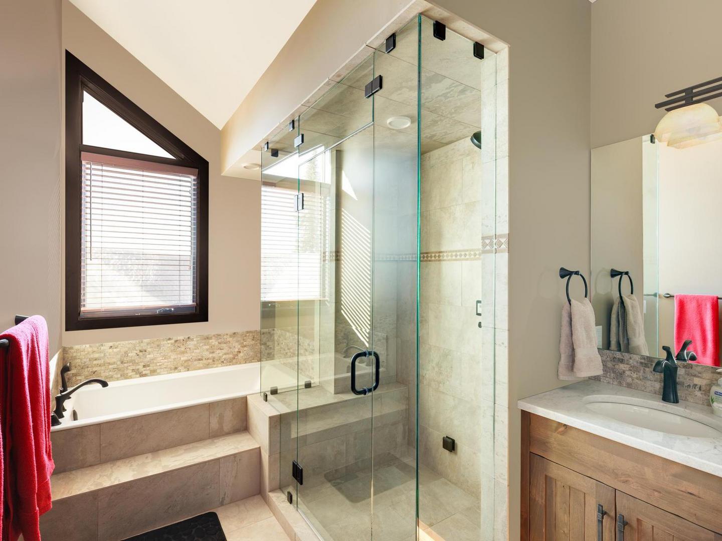 The luxury, spa-like master bedroom ensuite with a walk-in steam shower, soaker tub, bright natural light and high-end finishes in White Caviar at Big White Ski Resort.