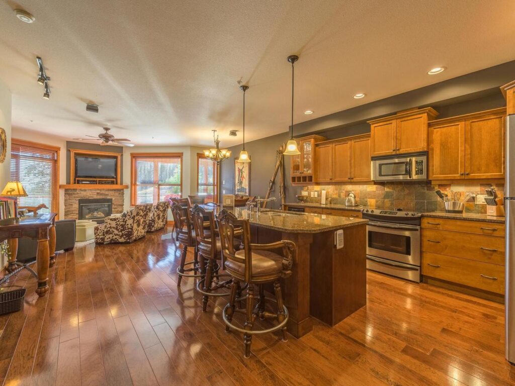 The open concept kitchen and dining area, with bright large windows in the background, hardwood floors and luxury finishes in one of the Snowbird Lodge luxury vacation rentals at Big White Ski Resort, managed by Luxury Mountain Vacation Rentals.