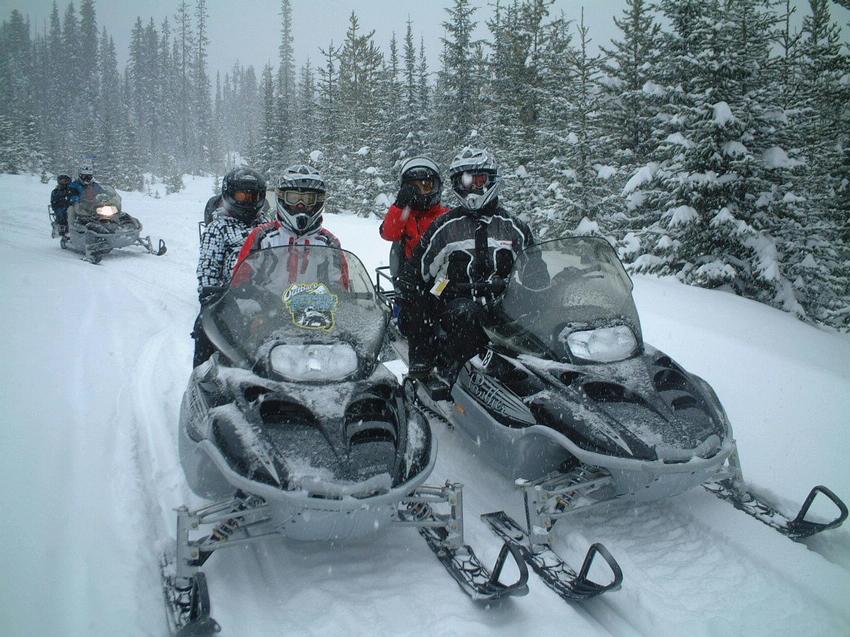 Two couples each ride a snowmobile along a snow covered path with snowcovered trees in the background as it continues to snow while at Big White Ski Resort.