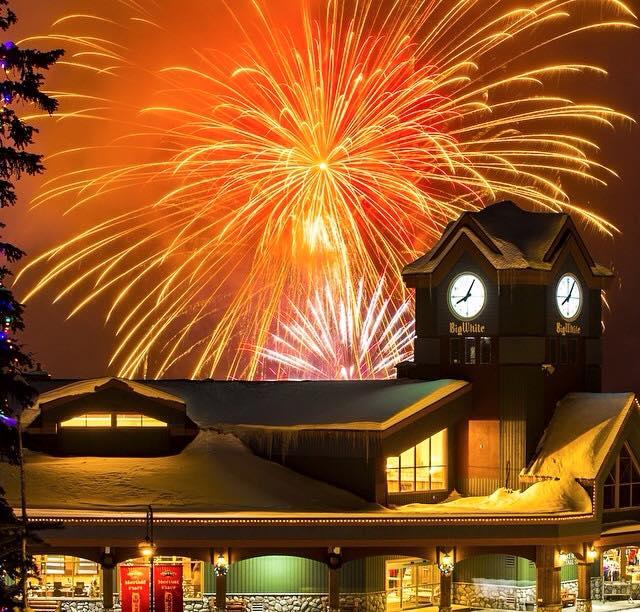 Orange and red fireworks burst overtop the large Big White Clock Tower in the Village Centre at Big White Ski Resort.