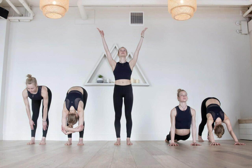 Five people are doing yoga, are stretching their bodies on a wooden floor.