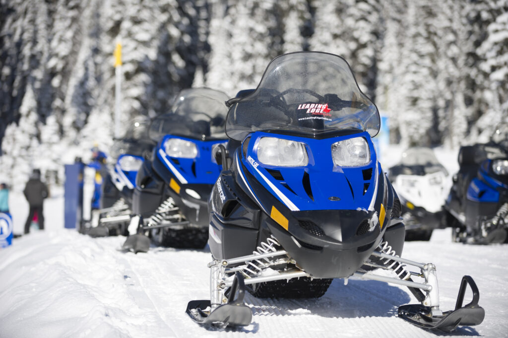 Blue snowmobiles parked organized. It is the winder season and there are trees with snow at the back.