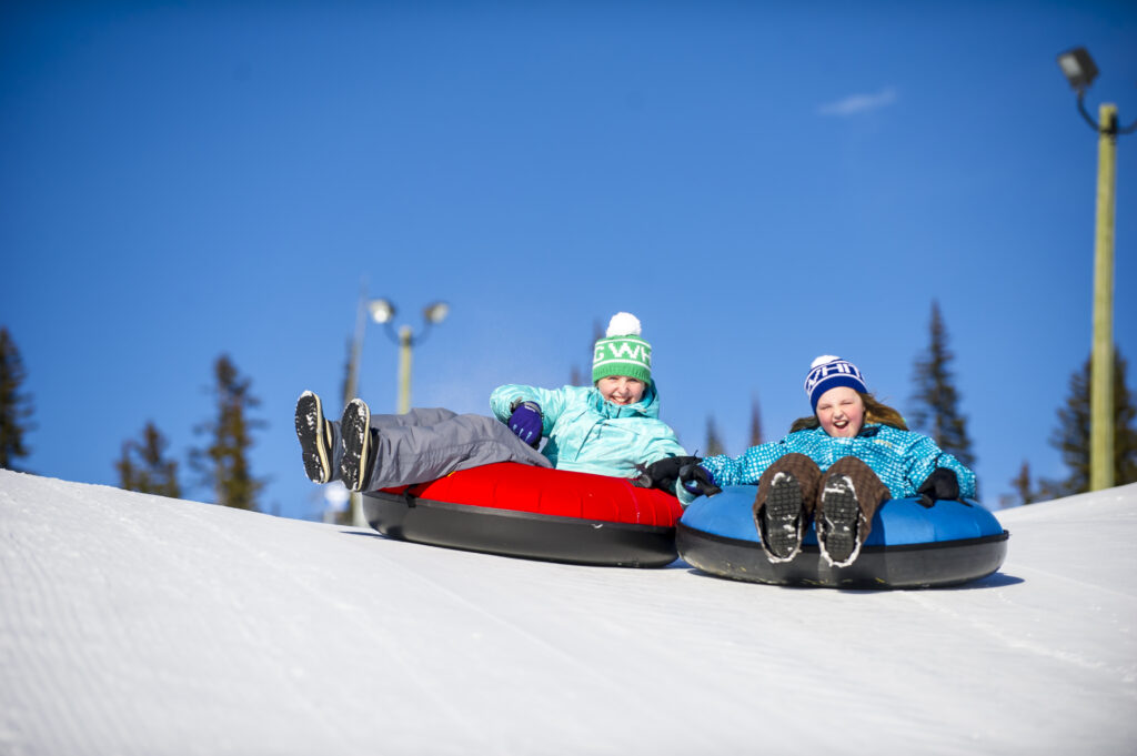 Two people are tubing on snow. They are wearing winter equipment to keep warm.