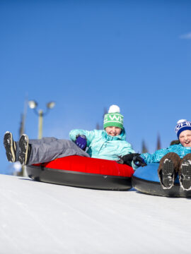 Two people are tubing on snow. They are wearing winter equipment to keep warm.