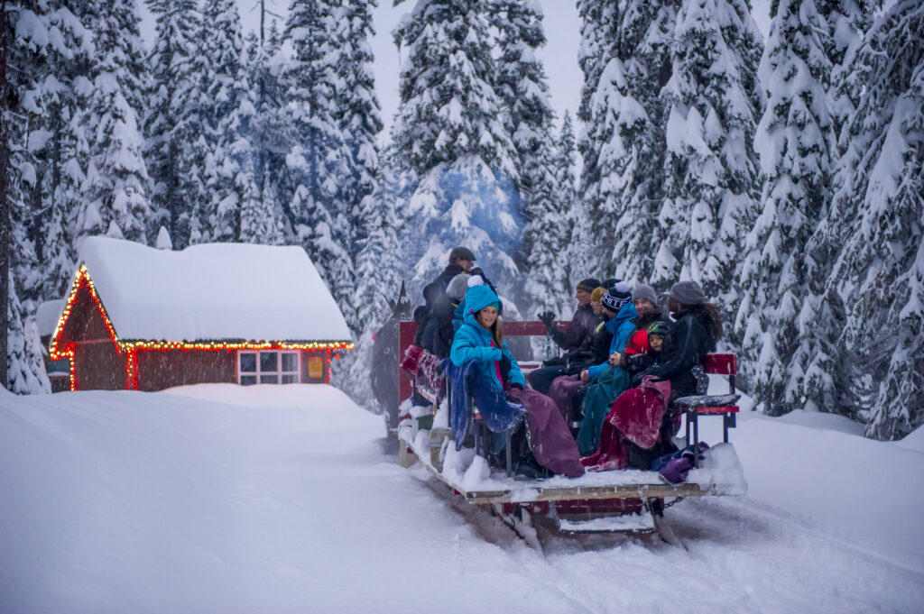 There is a family on a sleigh ride heading to a house covered in snow.