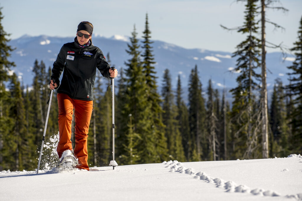 A person is snowshoeing, she is wearing organde pants and a dark jacket.