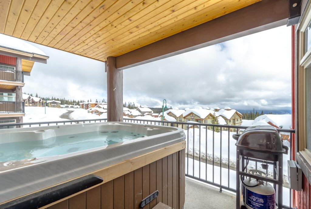 Hot tub on a private deck in a Luxury Mountain Vacation Rental Big White accommodation unit, overlooking snow-topped condos below
