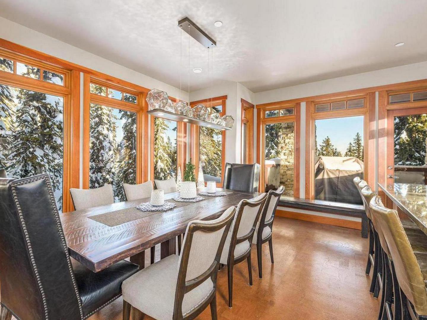Magnificent Moonshine's luxury dining room with a large table, panoramic windows and hardwood floors, managed by Luxury Mountain Vacation Rentals at Big White Ski Resort.