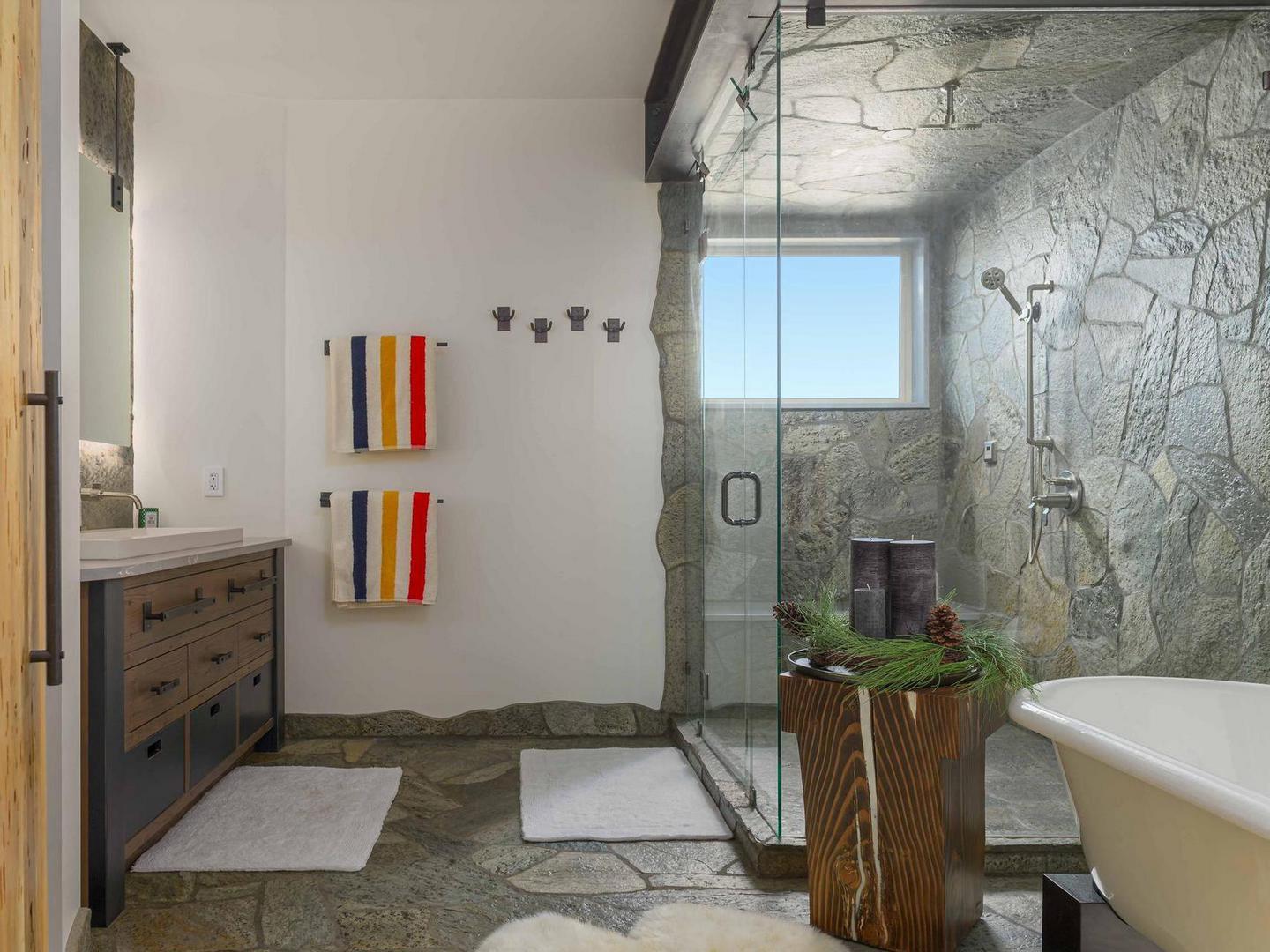 A large and spacious luxury bathroom with a walk-in shower and soaker tub, with stone accents and bright lighting, in one of Luxury Vacation Rentals' luxury properties at Big White Ski Resort.