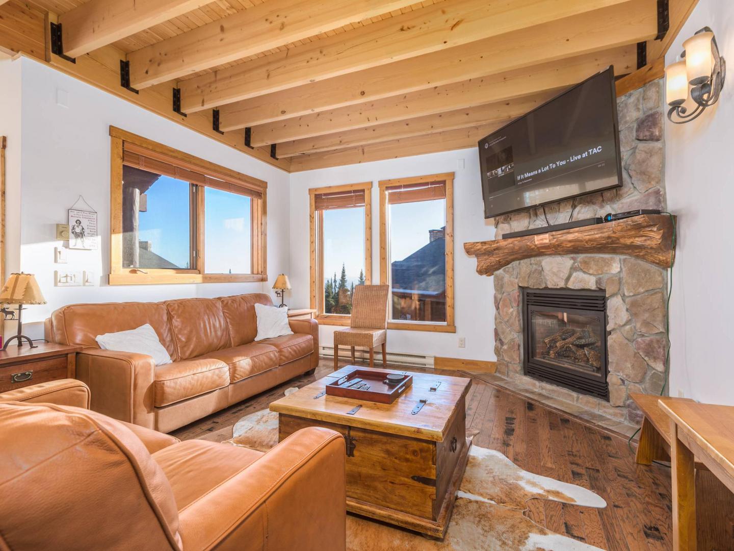 Aspen Meadows' modern living room with comfortable couches, bright natural light and a stone fireplace, managed by Luxury Mountain Vacation Rentals at Big White Ski Resort.