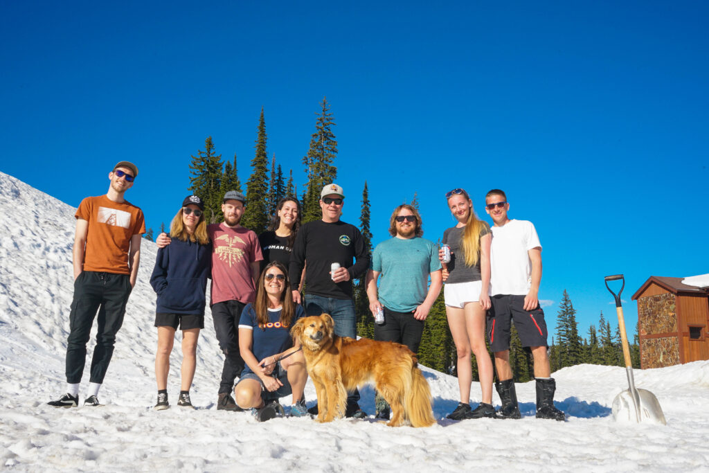 A group of LMVR staff members and a golden retriever stand in the snow at Big White on a blue-skied day