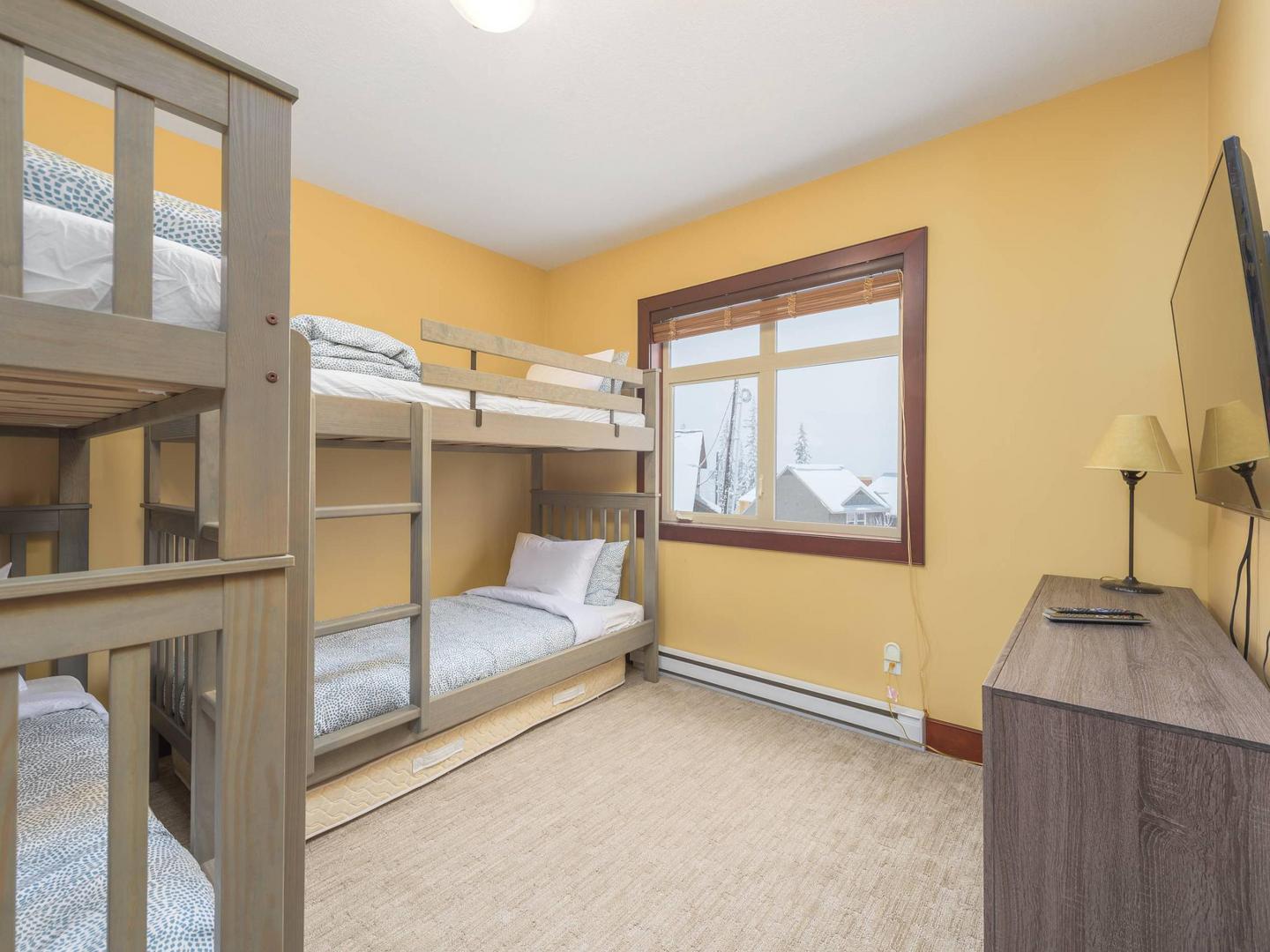 A bedroom with two single bunkbeds, each with two beds, in abrightly lit, cozy bedroom, perfect for the kids, in Aspens #6 luxury vacation rental at Big White Ski Resort.