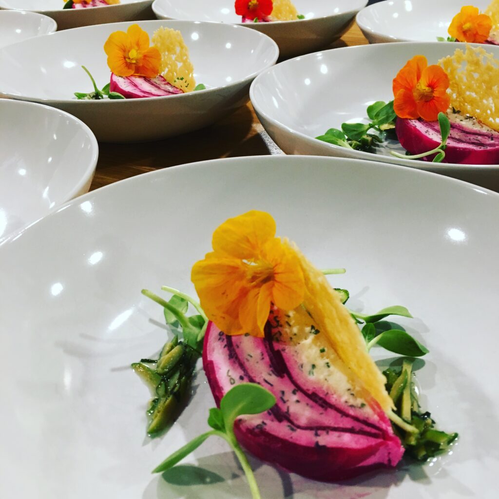 A plate of gourmet local ingredients made by Backyard Farm Chef's Table for a private culinary experience, with an orange flower on top of it.