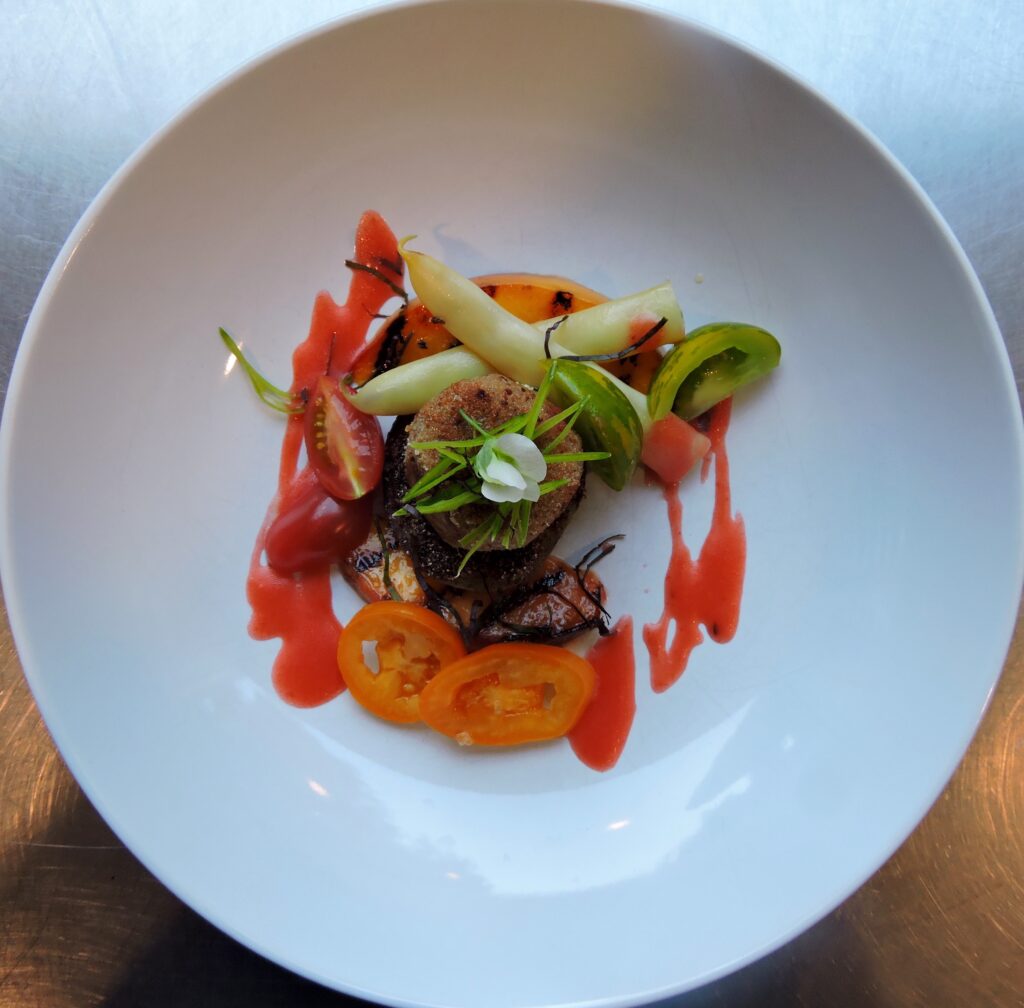 A plate of gourmet summer ingredients made by Backyard Farm Chef's Table for a private culinary experience, plated inside a bowl with bright oranges and reds and green ingredients.