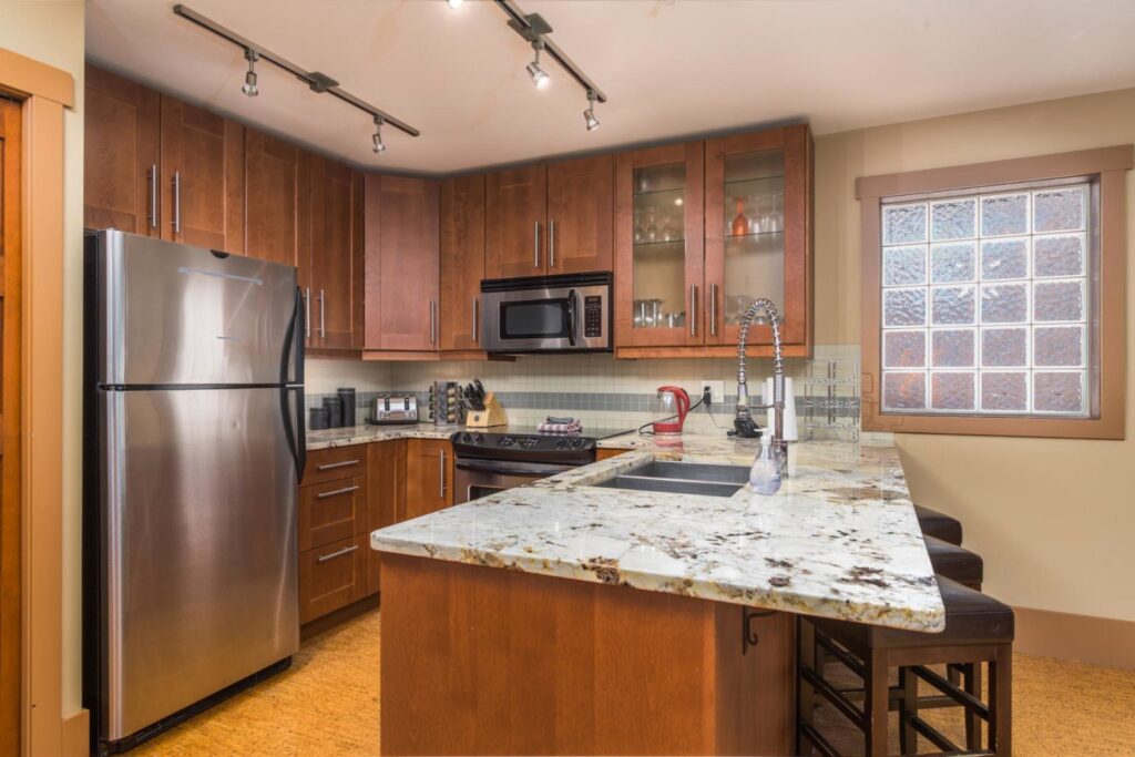 Pet-friendly Raven Unit 205's gourmet kitchen, with warm, chestnut coloured wooden cabinets, stainless steel appliances and marbled countertop.