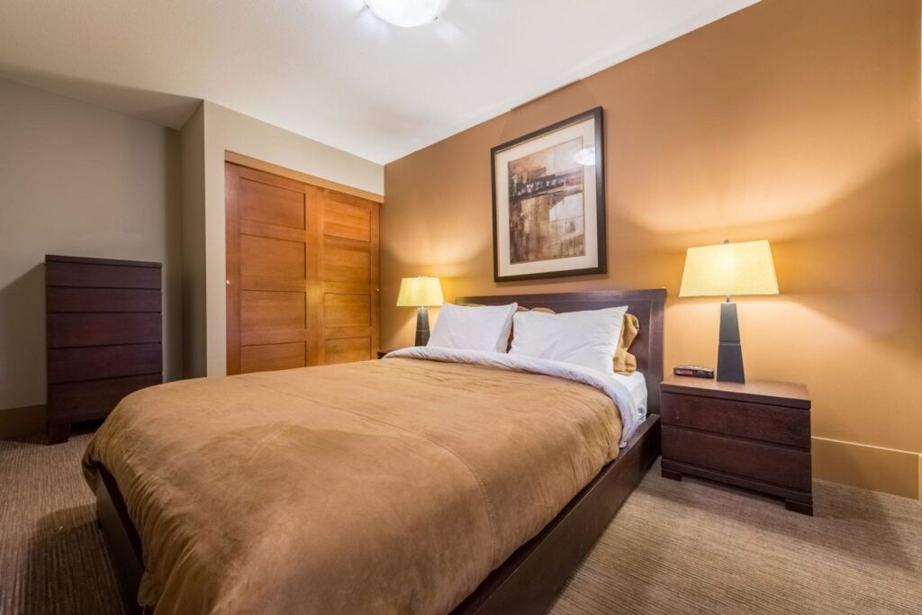One of the pet-friendly Raven Unit 209's comfortable, relaxing bedrooms, with a comfortable bed, carpeted floors, cozy blankets and bright lighting.