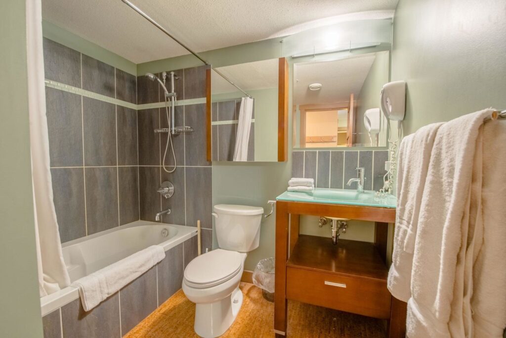 Pet-friendly Raven Unit 307's spa-like luxury bathroom, with a large bathtub, grey tiles, glass counters and wooden floors.