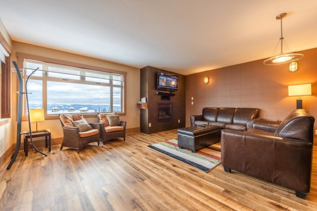 Pet-friendly Raven Unit 308's spacious, open living room, with comfortable seating, bright light from its large window, hardwood floors and a cozy fireplace.