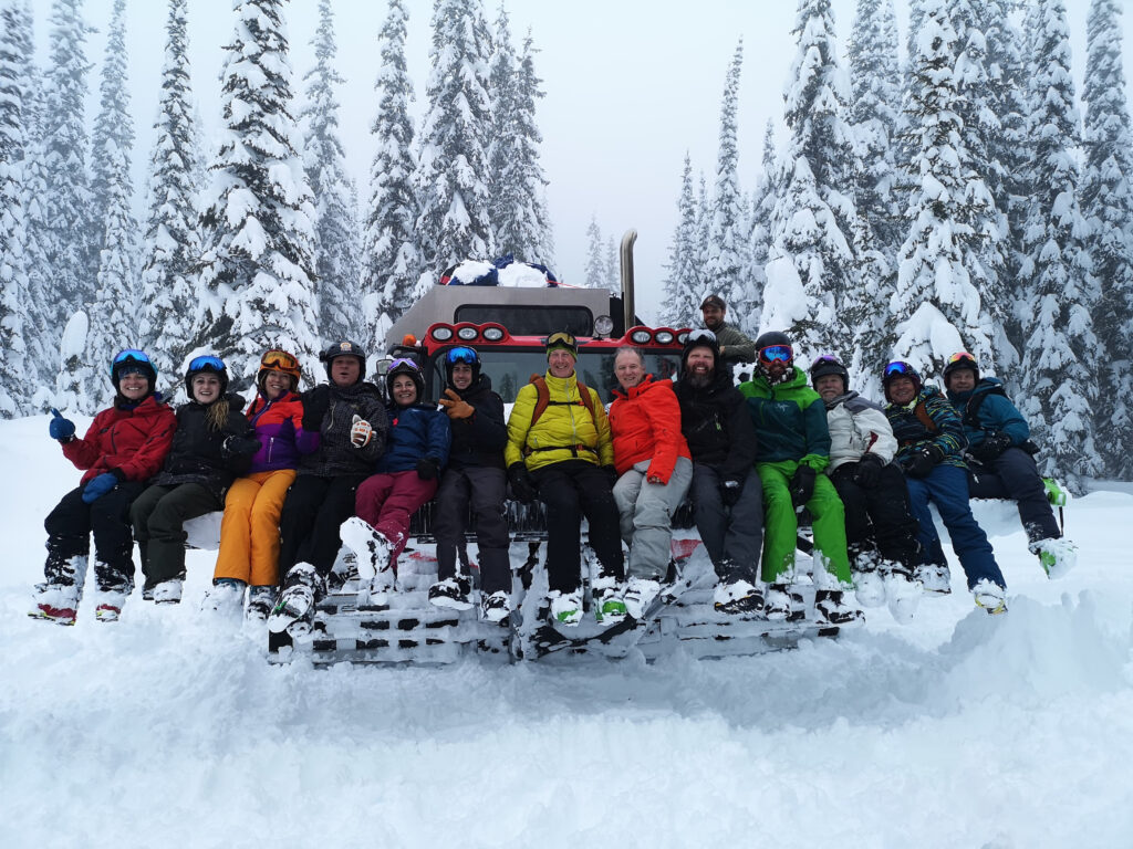 A group of cat skiers sitting on a Cat machine and posing for the photo, in snowy terrain with snow covered trees, on a excursion with K3 Cat Ski.