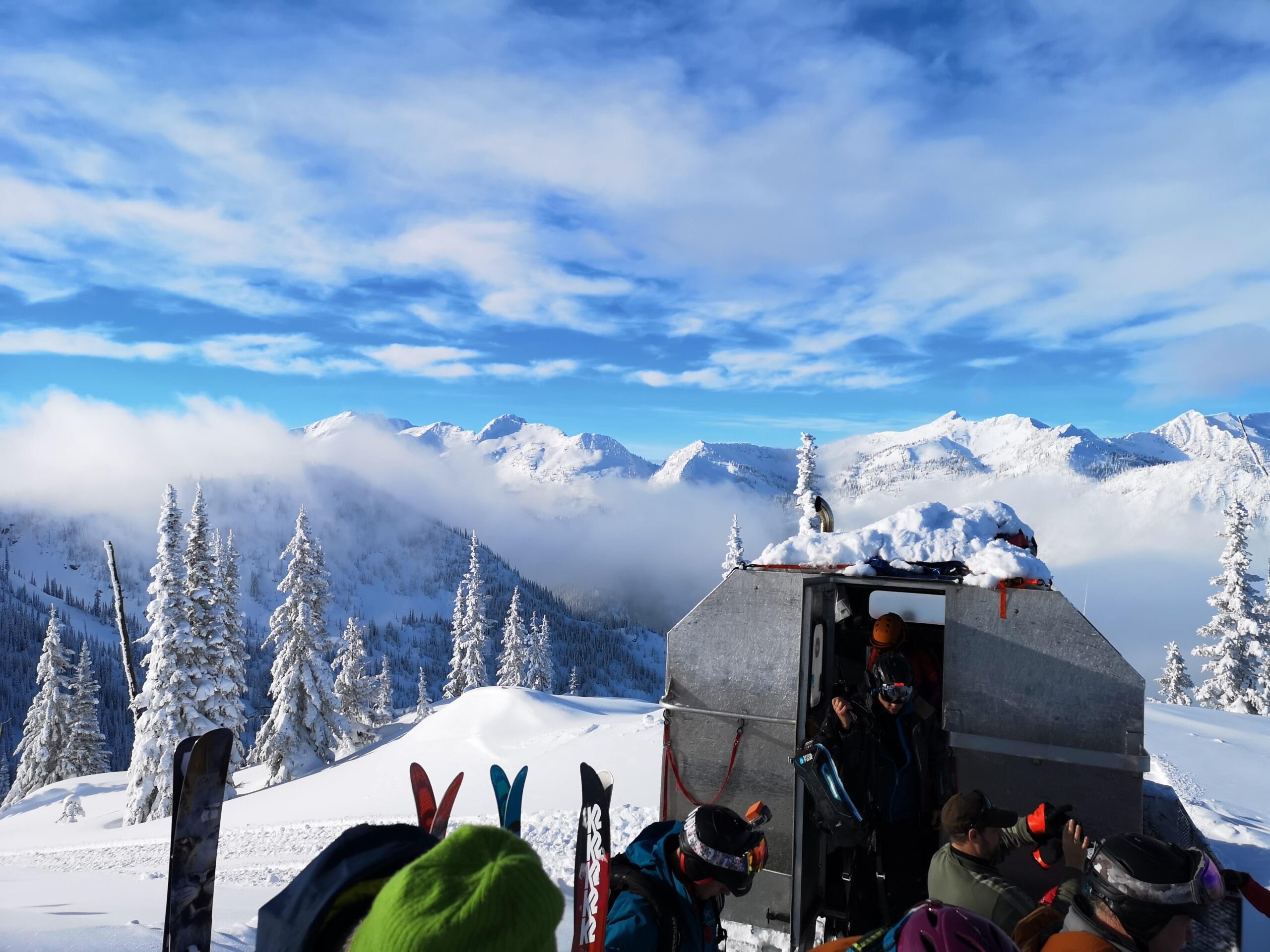 A group of skiers with K3 Cat Ski overlooking the snowy peaks of mountains over their skis.