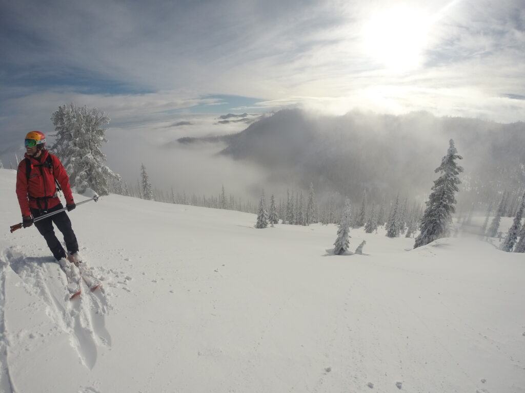 A lone cat skier poses on fluffy snowy terrain overlooking a snow-covered peak while on a trip with K3.