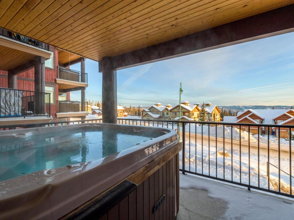 One of the Raven's private hot tubs on a private deck in the condo rental building, which overlooks Big White Ski Resort covered in snow, in a luxury rental suite operated by LMVR.