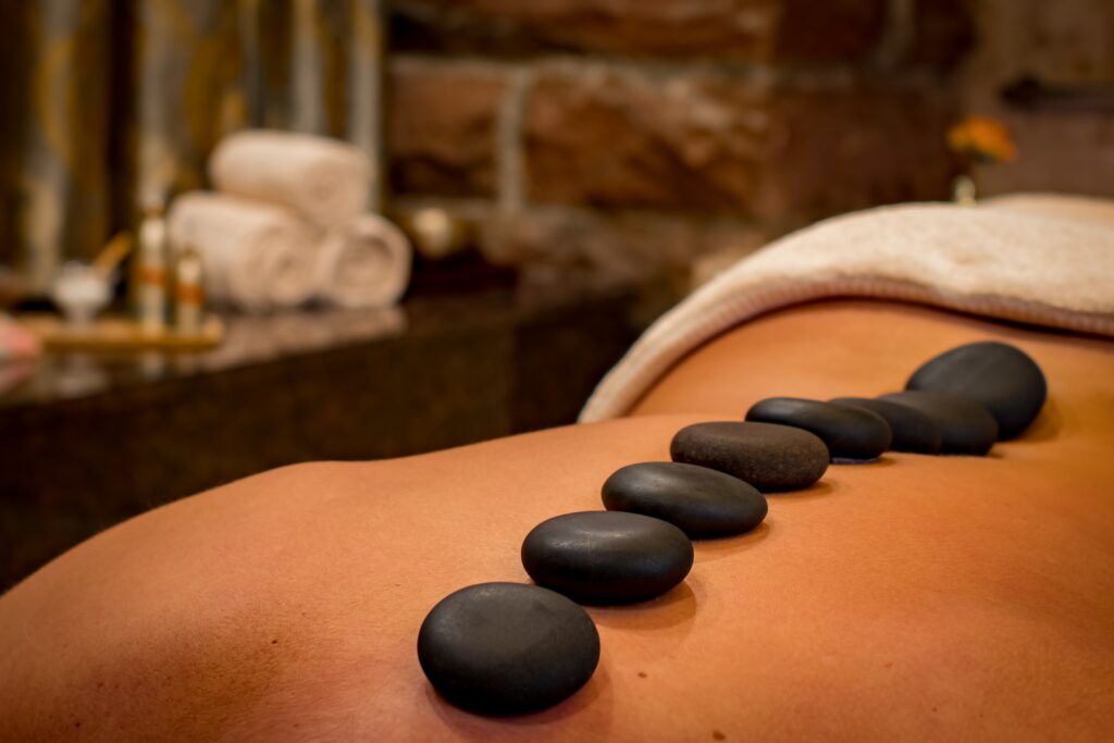 A hot stone massage with small black stones in a line along the spine of a person for a therapeutic, health & wellness experience that relieves stress and pain through expert techniques, heat and control, done with Big White Mountain Massage from a massage therapist. 
