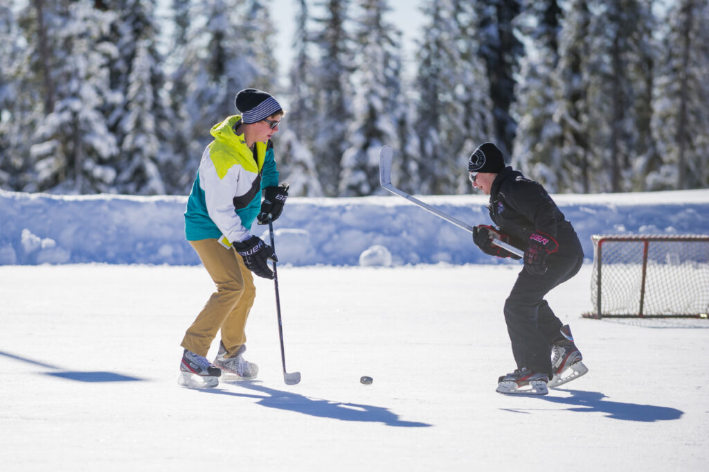 Two children skate and play ice hockey at Big White Ski Resort's ice skating rink, one of the highest outdoor skating rinks in Canada.