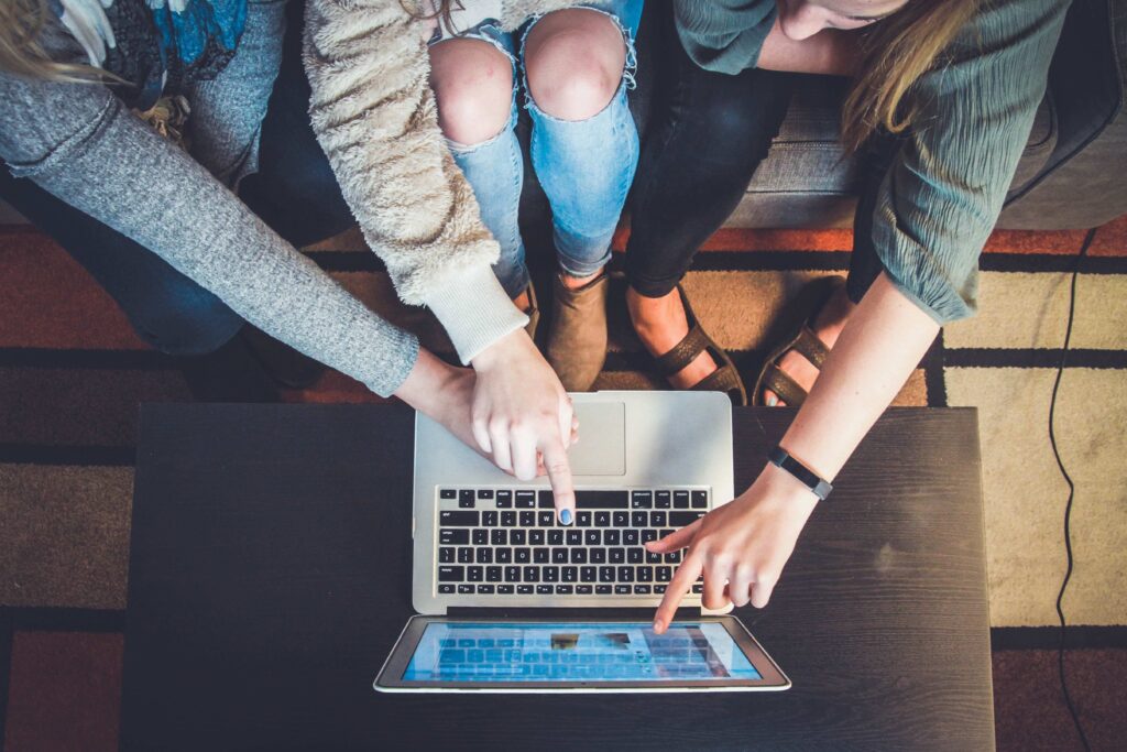 An overhead view of three people sitting on a couch and pointing at a laptop computer screen while booking a trip to go skiing in January at Big White Ski Resort