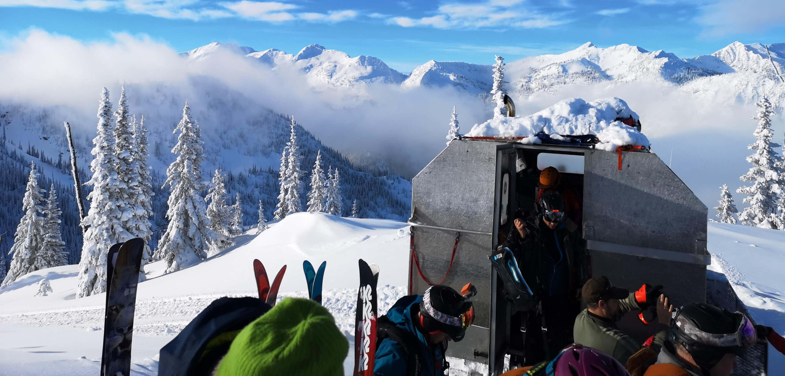 A group of skiers with K3 Cat Ski overlooking the snowy peaks of mountains over their skis.