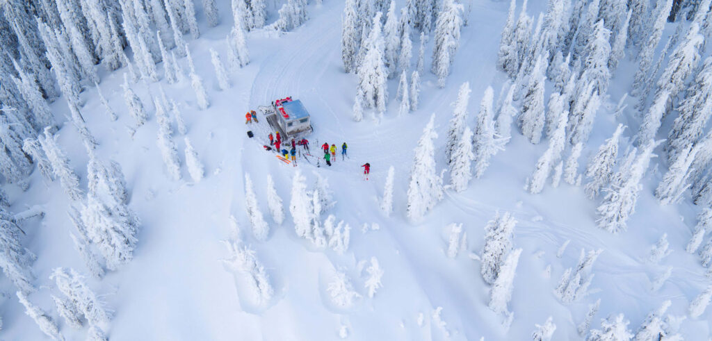 Birds eye view of cat machine with a group of skiers and guides as they traverse a snowy, white landscape of trees in Rossland area for Big Red Cats skiing