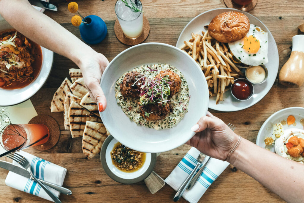 A bowl of food is being passed between two hands over a table of food.