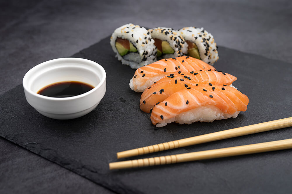 A plate of sushi with chopsticks and soy sauce sits on a charcoal table and plate.