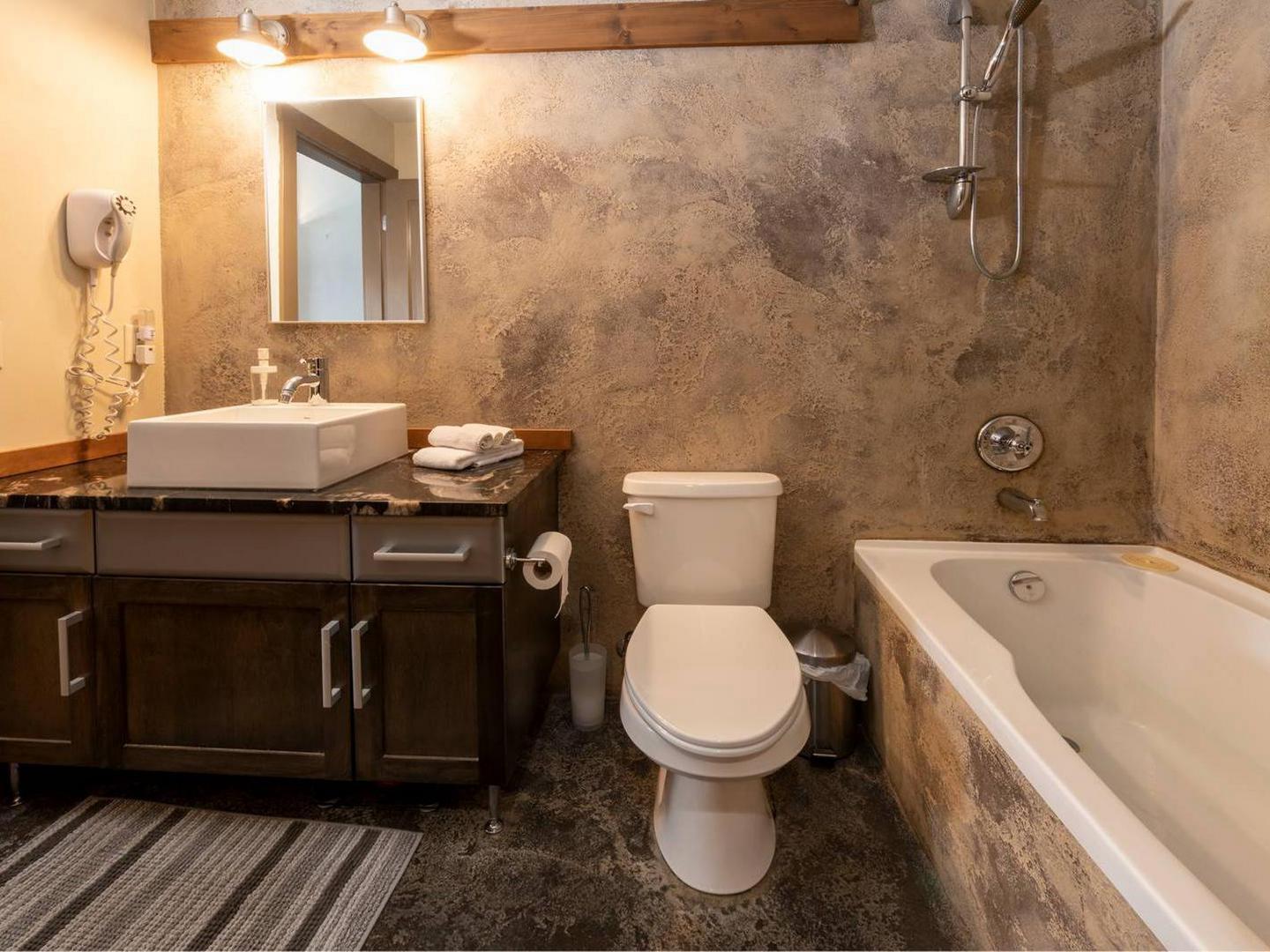 Timbers Penthouse Level condo rental luxury spa like bathroom with dark stone tile and a large soaker tub, managed by Luxury Mountain Vacation Rentals at Big White Ski Resort.