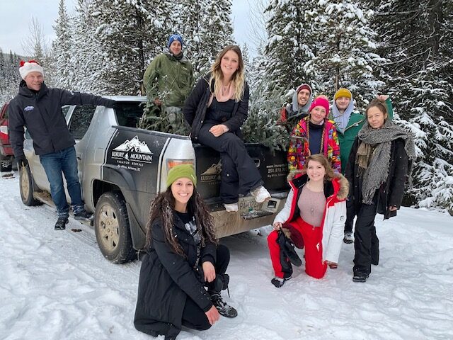 The Luxury Mountain Vacation Rentals' staff stand beside or sit on a large truck on a snowy day at Big White Ski Resort.