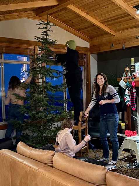 The Luxury Mountain Vacation Rentals staff stand around a pine christmas tree decorating it for Christmas at Big White Ski Resort.